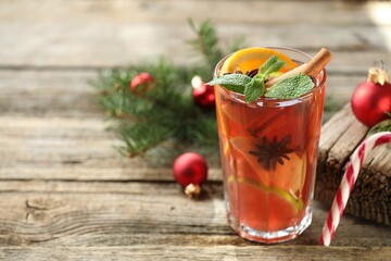 Tasty punch drink in glass, spices and Christmas decor on wooden table, closeup. Space for text