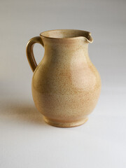 A rustic, speckled ceramic pitcher, light brown with an ergonomic handle, stands isolated on a bright background. Ideal for kitchen, home decor, or beverage serving.