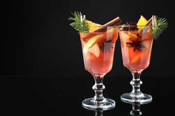 Tasty punch drink with spices in glasses on mirror surface against black background, closeup. Space for text