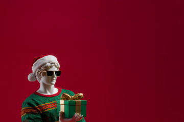 A statue of a Greek god holding a gift box. A man in a knitted sweater holding a Christmas present.