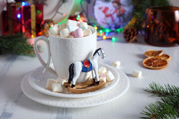 A decorative rocking horse figurine next to a cup of marshmallows against a festive New Year's table backdrop.