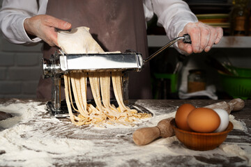 Caucasian female hands making fettuccine noodles using mechanical pasta machine