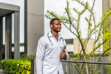 A smiling african american doctor in a white coat walks on the hospital rooftop, holding a tablet. He exudes confidence and positivity, showcasing the spirit of modern healthcare professionals.
