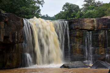 A wide waterfall of turbid water over a rocky ledge.