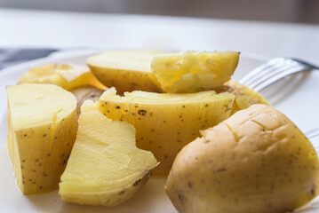 Fresh boiled potatoes cooked in skin, closeup photo. Boiled potato halves on white plate with natural light from window