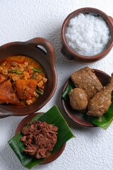 Gudeg or gudheg, Chicken bacem, egg bacem and tempeh bacem, spicy beef skin crackers or sambal krecek and salty porridge on whit background. Traditional food from Yogyakarta, Indonesia. Bubur gudheg