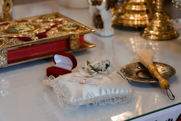 Wedding rings displayed on white satin pillow with floral arrangement and ornate religious artifacts in church setting