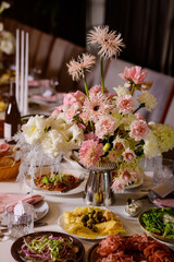A beautiful floral centerpiece with pink gerberas graces an elegantly set banquet table laden with gourmet appetizers for a festive celebration.