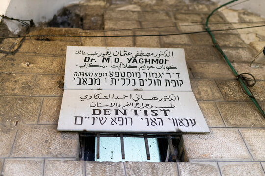 A multi-lingual sign in arabic, english, and hebrew for a dentist's office, "dr. m.o. yaghmour" (dentist), mounted on an ancient stone wall.
