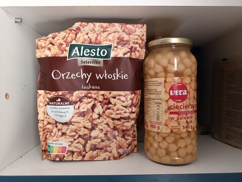 Alesto" brand bag of "Orzechy włoskie" (walnuts) and "Vera" brand jar of "cieciera" (chickpeas) displayed side-by-side on a home pantry shelf, highlighting common kitchen staples