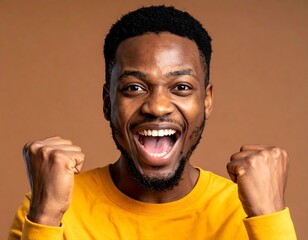 Close-up of an excited man with hands clenched in fists, beaming with a wide smile and open mouth. He wears a yellow shirt