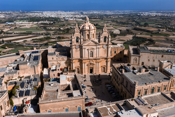 Obraz premium Aerial view of Mdina, Malta shows St. Pauls Cathedral, palazzi, and bastion walls amid fields to the Mediterranean in bright midday light with crisp warm stone