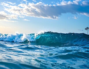 Close-up of an ocean wave crashing over, displaying a translucent turquoise hue under a sunny, partly cloudy blue sky