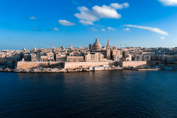 Fototapeta premium Aerial wide angle view of Valletta, Malta at sunset shows Grand Harbour, the basilica dome and cathedral spire above limestone bastions and Baroque buildings in warm light.