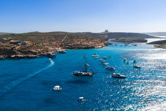 Aerial summer view of the Blue Lagoon in Malta, between Comino and Cominotto, with Saint Marys Tower, boats and swimmers moving in clear turquoise water in bright daylight.