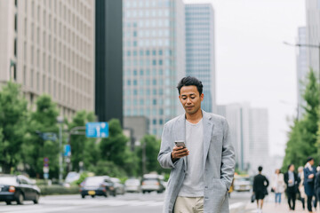 街を歩く午後 ― スマートフォンを見るビジネスカジュアルの男性
