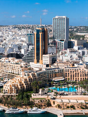 Aerial midday view of Sliema and St. Julian's, Malta, with Portomaso Marina, Hilton Malta, yachts, Portomaso Business Tower, and Mercury Tower under bright Mediterranean light. © Aerial Film Studio
