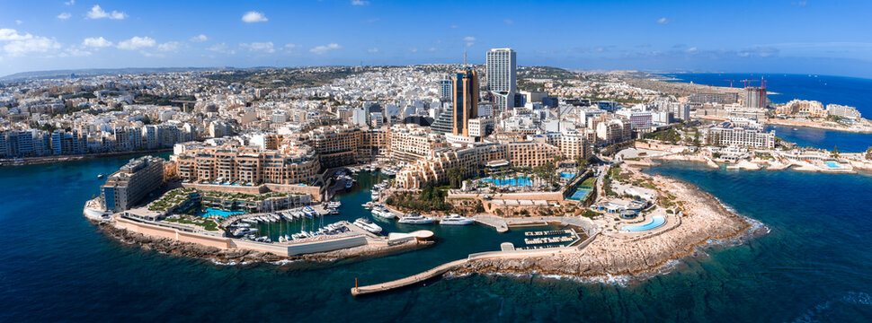 Aerial view shows Sliema and St. Julian's waterfront in Malta, with Portomaso Marina and Portomaso Business Tower, limestone buildings, piers, and midday light.