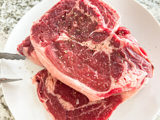 Close-Up of Two Raw Seasoned Ribeye Steaks