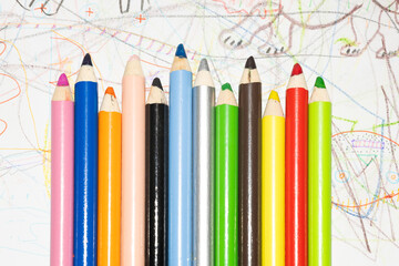 Multicolored pencils for drawing on white paper with children's drawings.