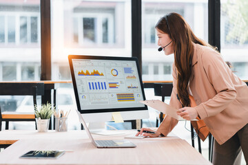 Businesswoman with headset analyzing sales performance dashboard on computer in modern office
