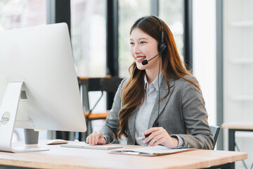 Young female customer service representative smiling at computer with headset providing friendly...