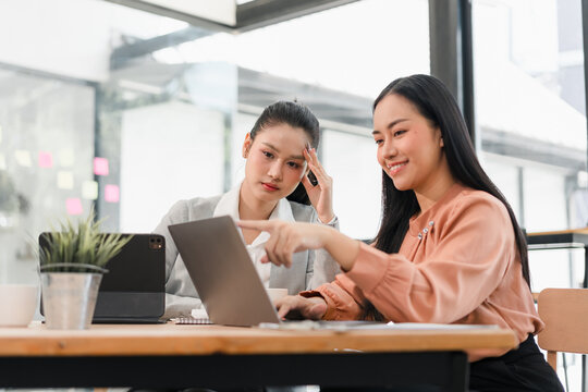 Young businesswoman and colleague collaborating on laptop in modern office, focused and engaged