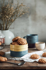 Fototapeta premium Homemade cookies in a metal tin on rustic wooden table with mugs and dried flowers — cozy home baking and snack concept