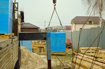 A crane truck unloads building blocks wrapped in blue film.