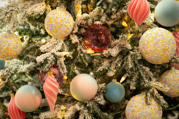 Pastel Christmas ornaments and lights on snowy fir branches