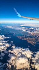 Fototapeta premium Aerial view from an airplane window showing mountains, clouds, and a bright blue sky