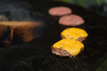 Juicy cheeseburgers with melting cheese grilling over open fire