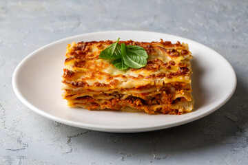 Portion of ground beef lasagna topped with melted cheese and garnished with fresh parsley served on a plate in close view for a menu