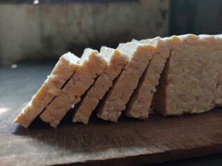 Raw tempeh slices on the wooden cutting board.