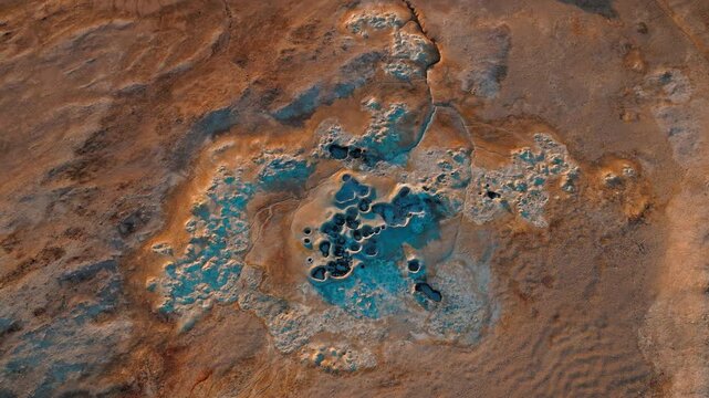 Top-down drone footage of boiling mud pools in Hverir geothermal area, North Iceland. The hot springs form circular mineral patterns.