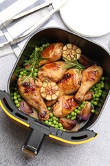 Fototapeta premium Air fryer basket with grilled chicken drumsticks, spices, green peas and tongs on grey table, flat lay