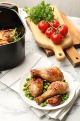 Grilled chicken drumsticks and air fryer basket with meal on white marble table
