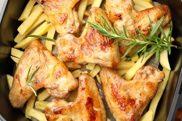 Grilled chicken wings and french fries with rosemary in air fryer basket, closeup