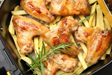 Grilled chicken wings with french fries and rosemary in air fryer basket on table, top view