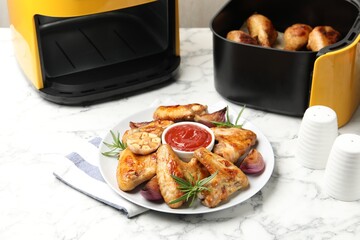 Delicious grilled chicken wings, sauce and spices near air fryer with cooked drumsticks on white marble table