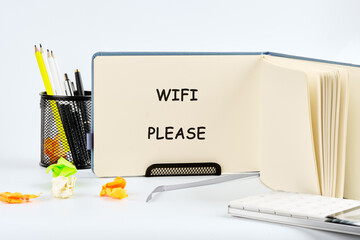 An open notebook shows the words WIFI PLEASE written in simple black letters. A pencil holder with pens and pencils is visible, alongside crumpled colorful papers
