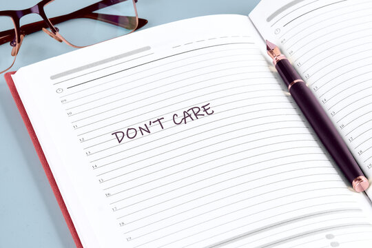 An open day planner with the words Dont Care written across the page. A pen rests near the binding and glasses sit in the upper left corner, suggesting a carefree attitude