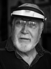 Elderly man with magnifying visor smiling while engaged in detail-oriented crafting activity indoors