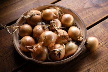 Freshly harvested onions in a rustic bowl resting on a wooden table in natural light