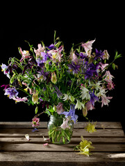 Colorful bouquet of wildflowers in a glass jar on a wooden table against a dark background