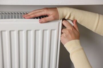 Woman adjusting temperature of radiator indoors, closeup