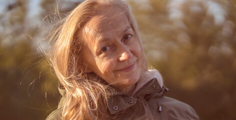 Old cheerful woman with a smiiley face walks in the city in the autumn sunny day.