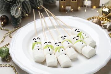 Christmas food. Funny snowmen made of marshmallows and decor on beige table, closeup