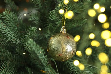 Christmas bauble and festive lights hanging on fir tree branch, closeup. Bokeh effect