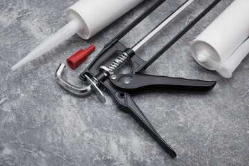The sealant gun with spare tube or cartridges for caulking and home repair work. The adhesive sealing tools on gray background with copyspace area for captions.